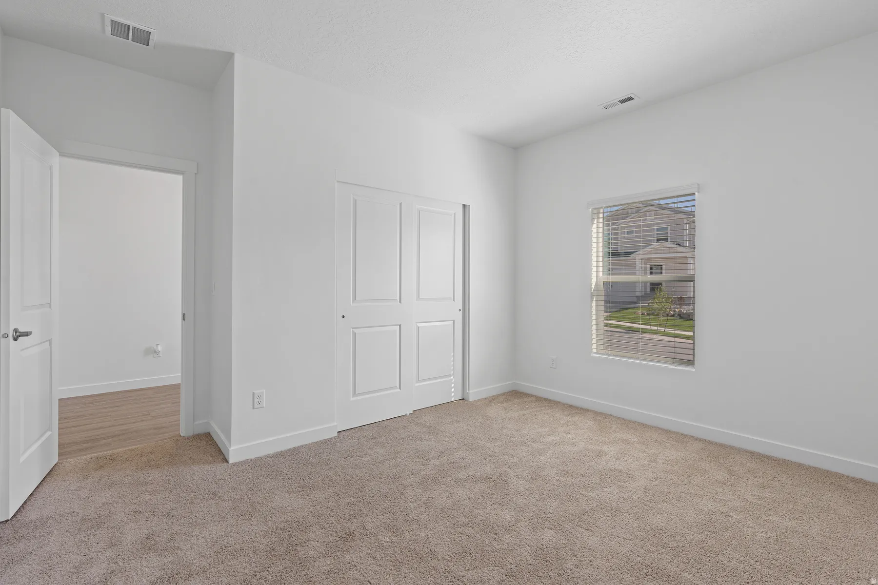 Neutral-toned carpeting, white interior walls, window with horizontal blinds, and a bi-fold closet door