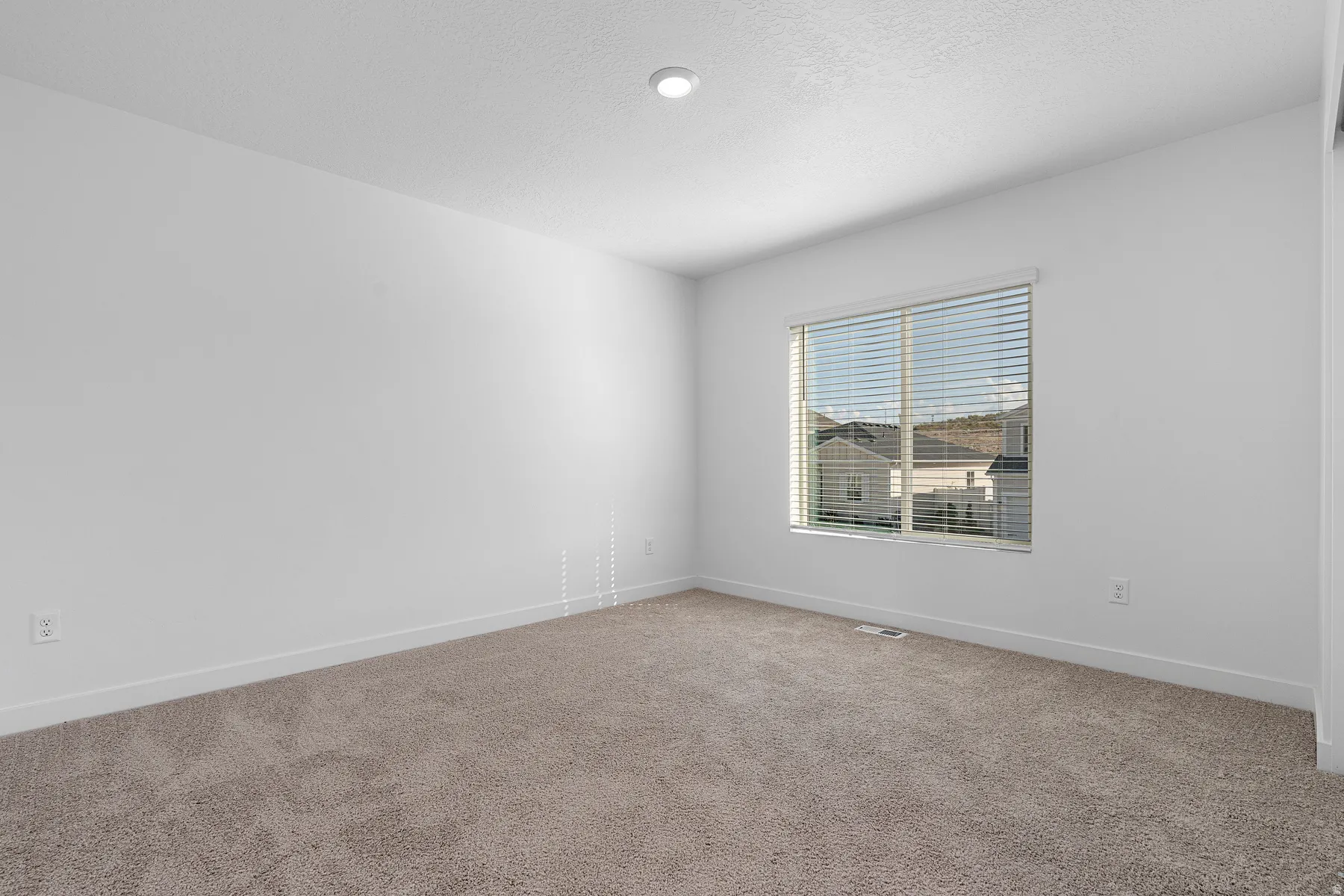 Bright bedroom featuring neutral carpet flooring, recessed ceiling lighting, and large double-hung window with horizontal blinds offering natural illumination
