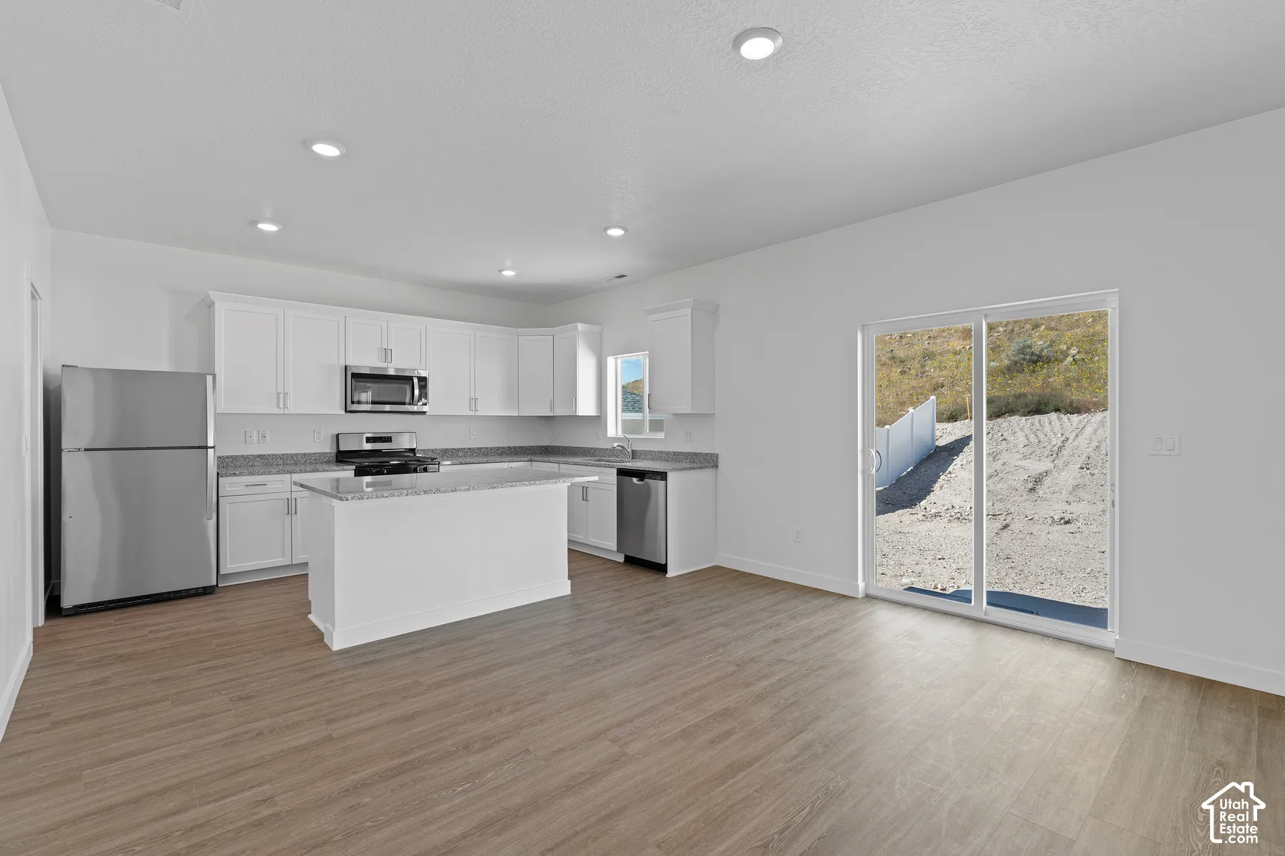 Open-concept kitchen with white cabinetry, stainless steel appliances, granite countertops, and a central island