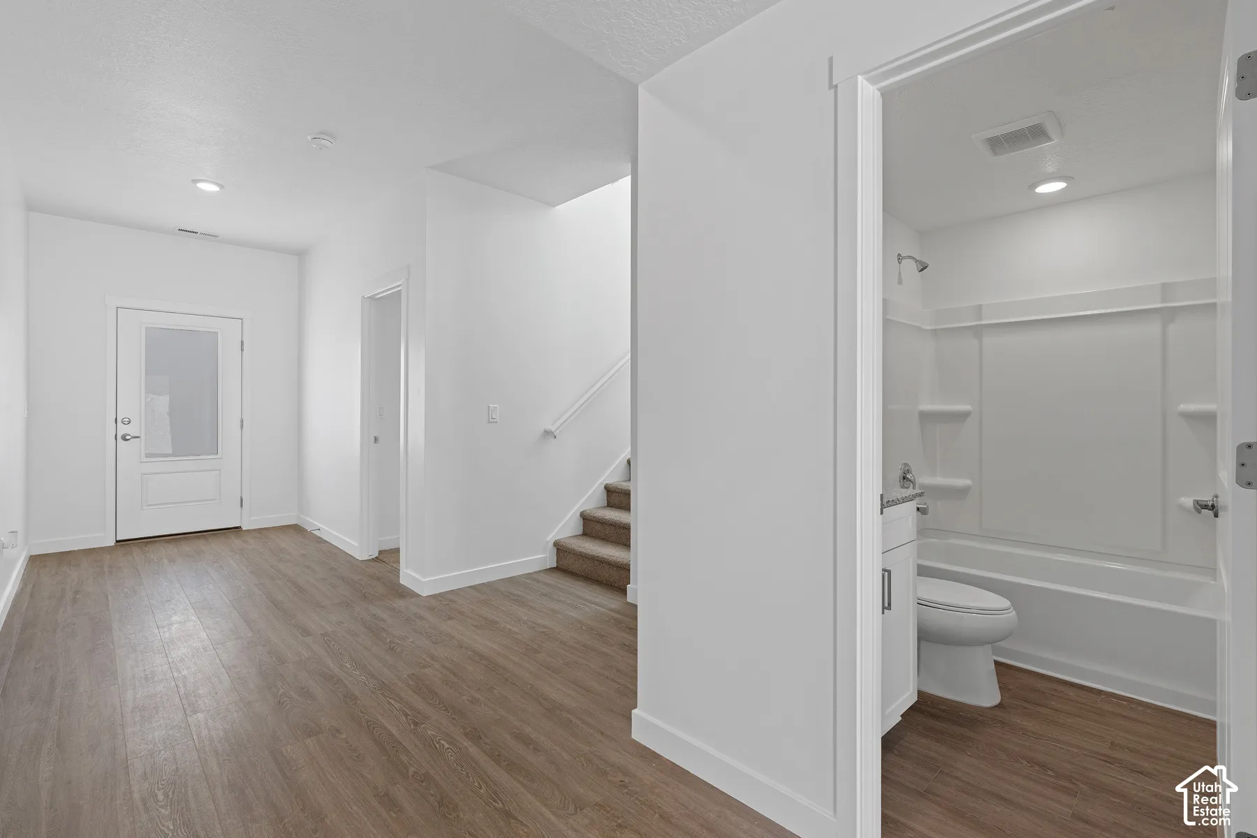 Wood-finish flooring, recessed lighting, white interior doors, staircase with carpeted treads, and a full bathroom with a tub/shower combination