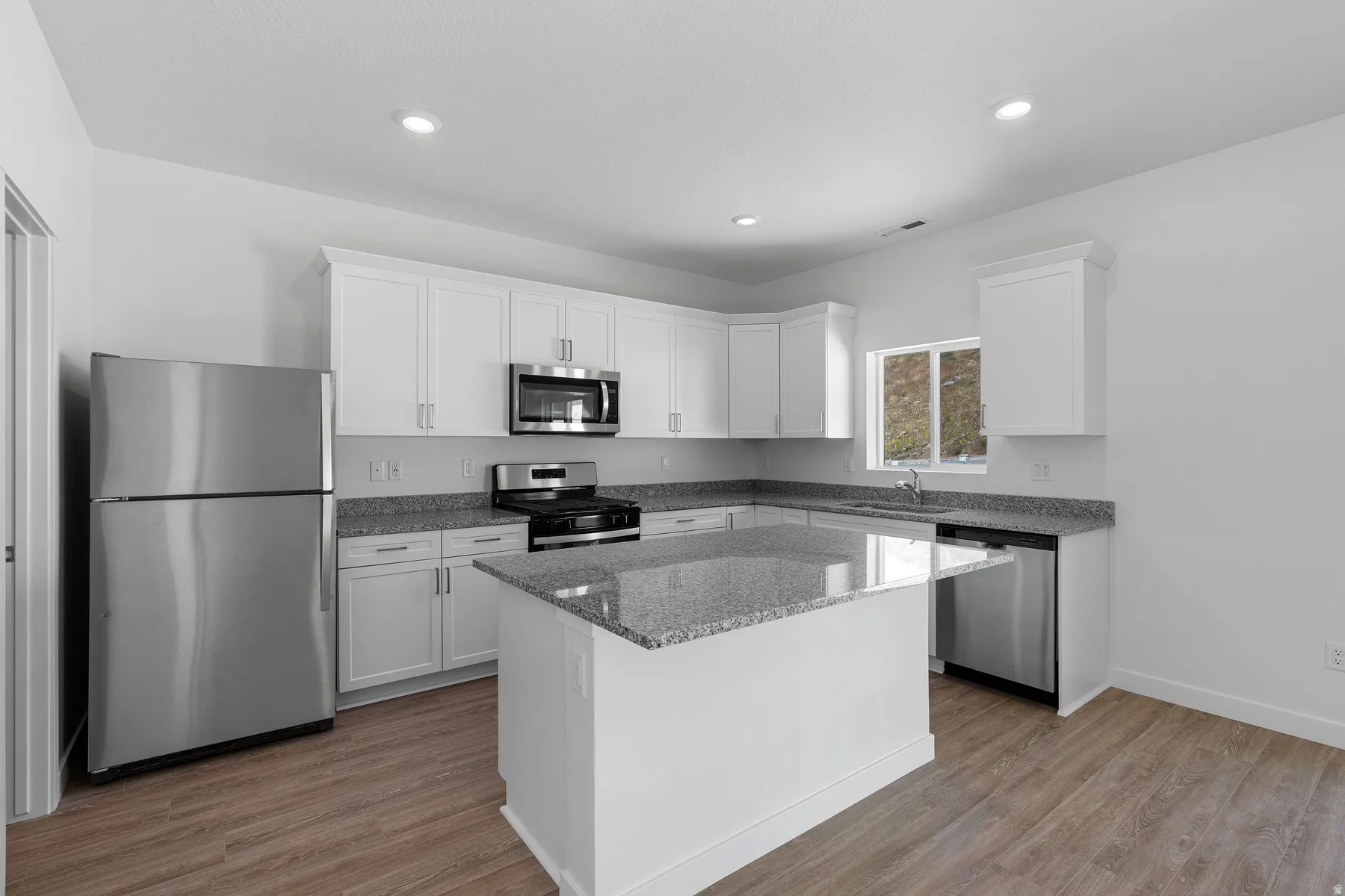 Kitchen featuring white cabinetry, granite countertops, stainless steel appliances, a kitchen island, and wood-finish flooring
