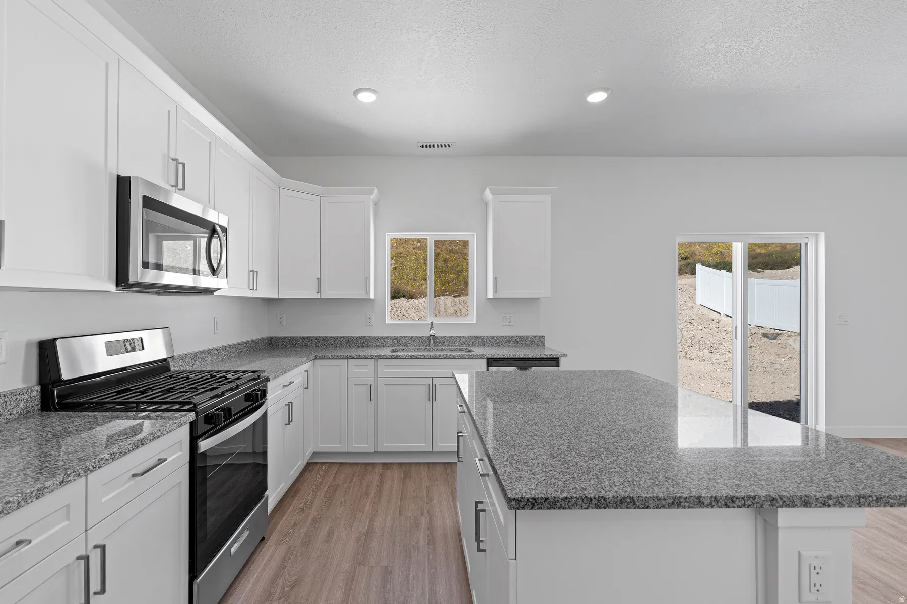 Contemporary kitchen featuring white cabinetry, stainless steel appliances, wood-finish flooring, granite countertops, and a kitchen island