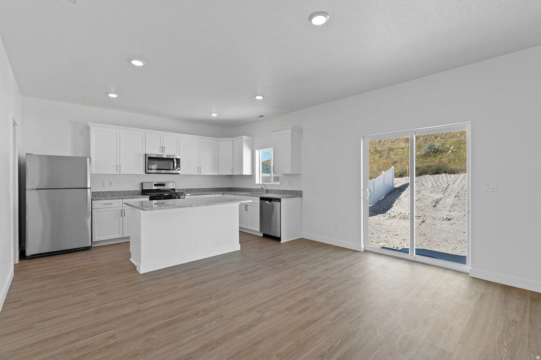Open-concept kitchen with white cabinetry, stainless steel appliances, granite countertops, and a central island