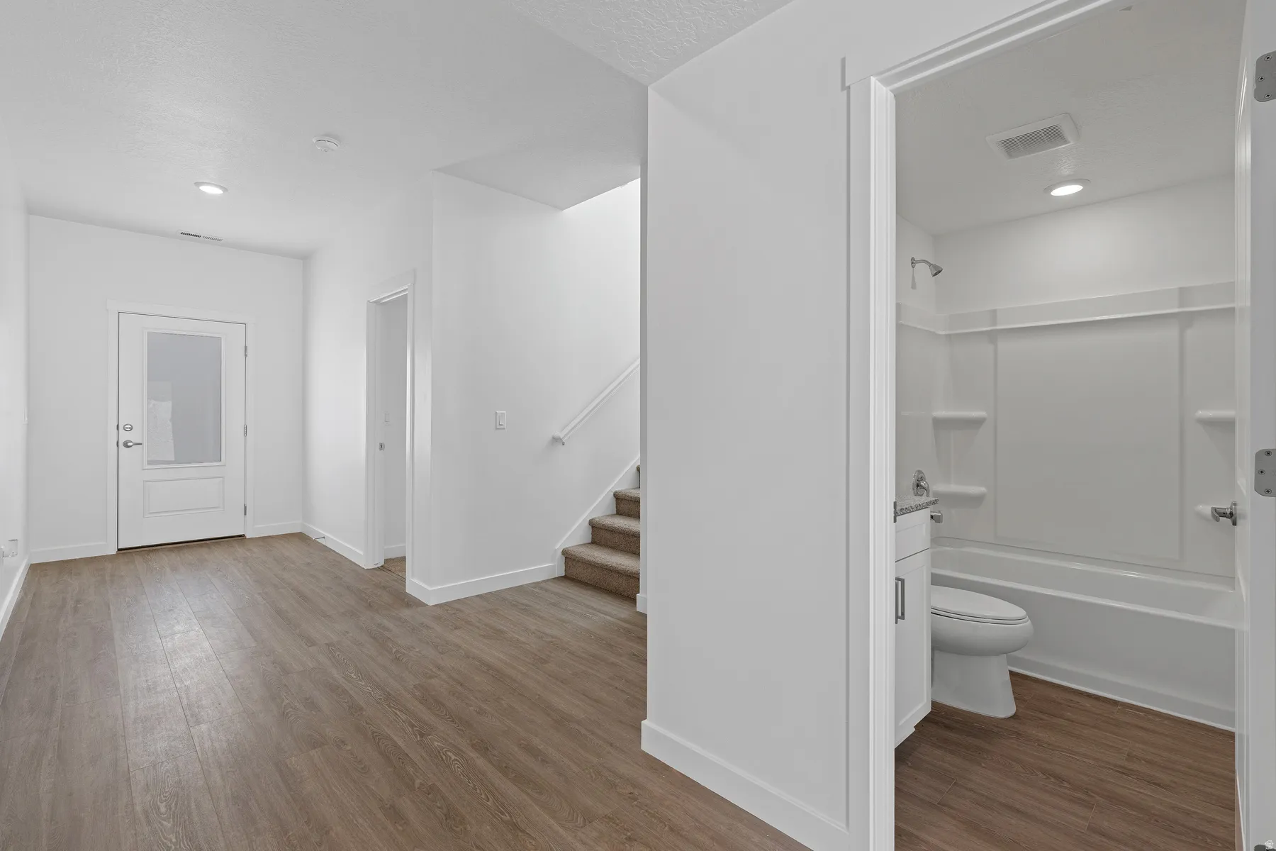 Wood-finish flooring, recessed lighting, white interior doors, staircase with carpeted treads, and a full bathroom with a tub/shower combination