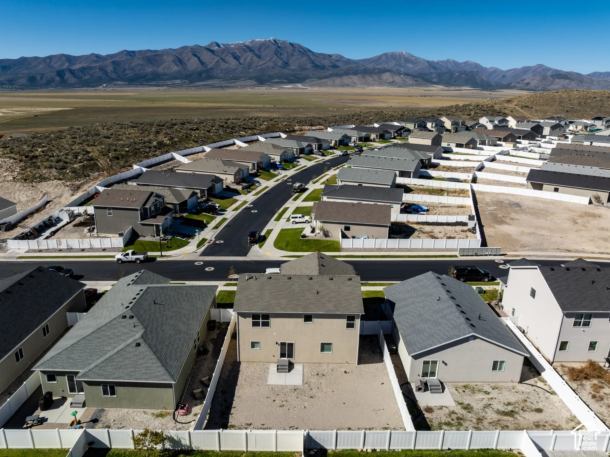 Aerial perspective featuring suburban residential development, multi-story home exteriors, concrete rear patios, white vinyl perimeter fencing, and prominent mountain backdrop