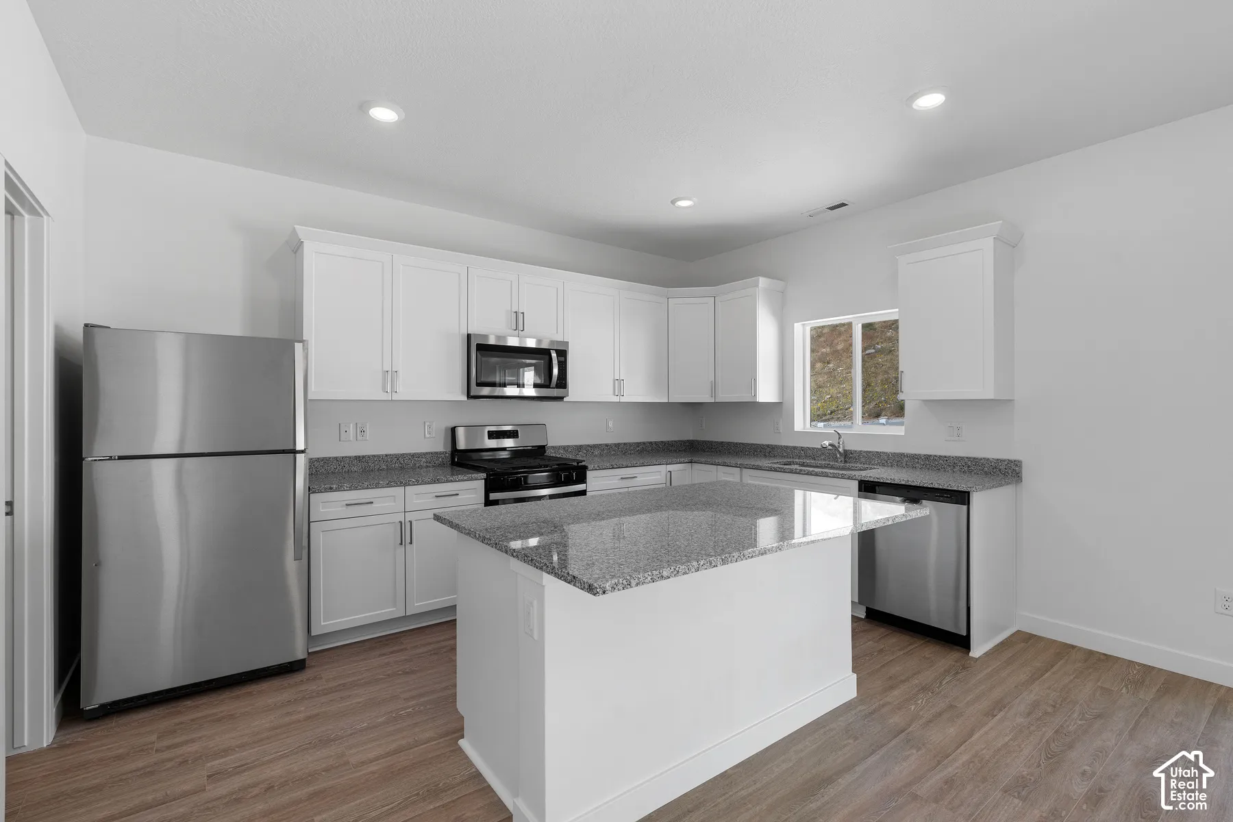 Kitchen featuring white cabinetry, granite countertops, stainless steel appliances, a kitchen island, and wood-finish flooring