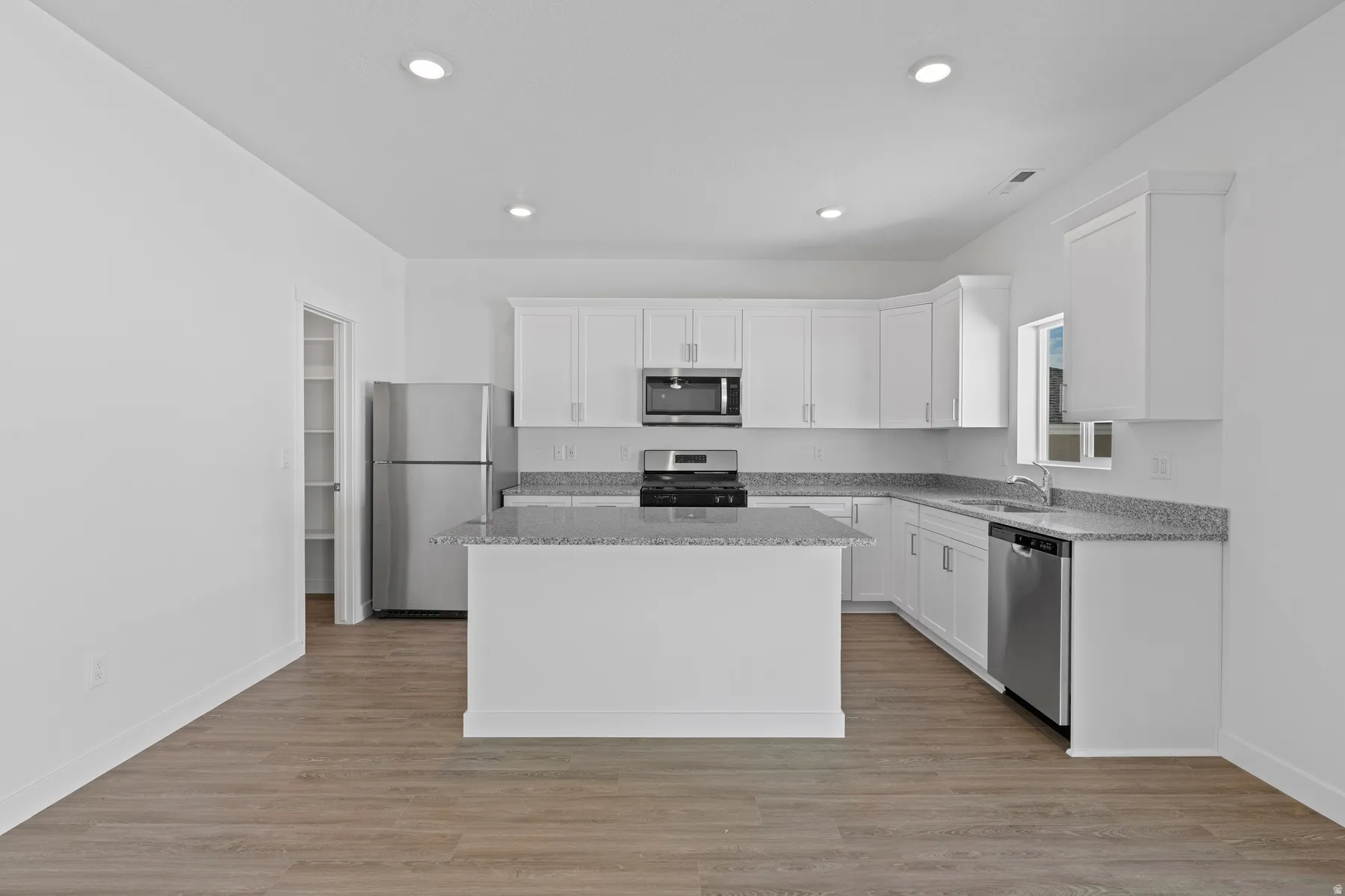Kitchen featuring white cabinetry, stainless steel appliances, a center island, and wood-finish flooring