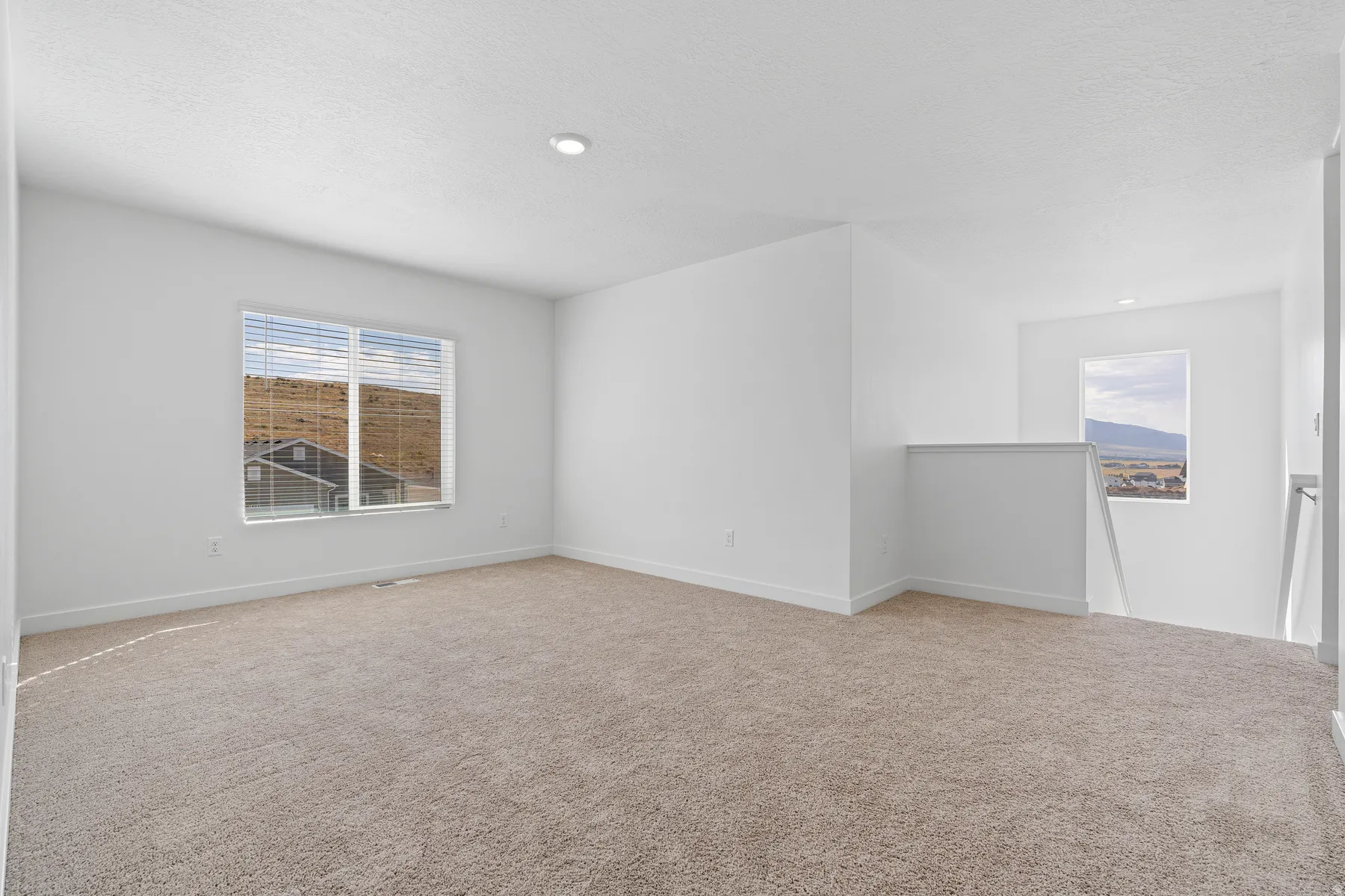 Carpeted open-concept room featuring white walls and a large window with horizontal blinds