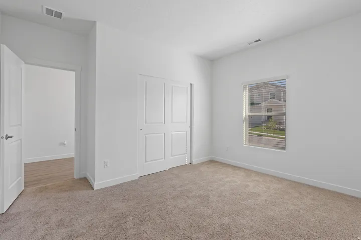 Neutral-toned carpeting, white interior walls, window with horizontal blinds, and a bi-fold closet door