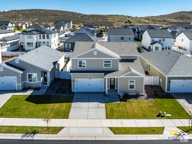 Two-story residence featuring vertical siding, a front-facing attached two-car garage, concrete driveway, and xeriscaped front garden beds with a manicured lawn
