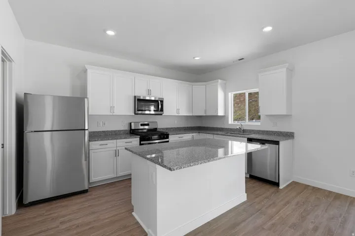 Kitchen featuring white cabinetry, granite countertops, stainless steel appliances, a kitchen island, and wood-finish flooring
