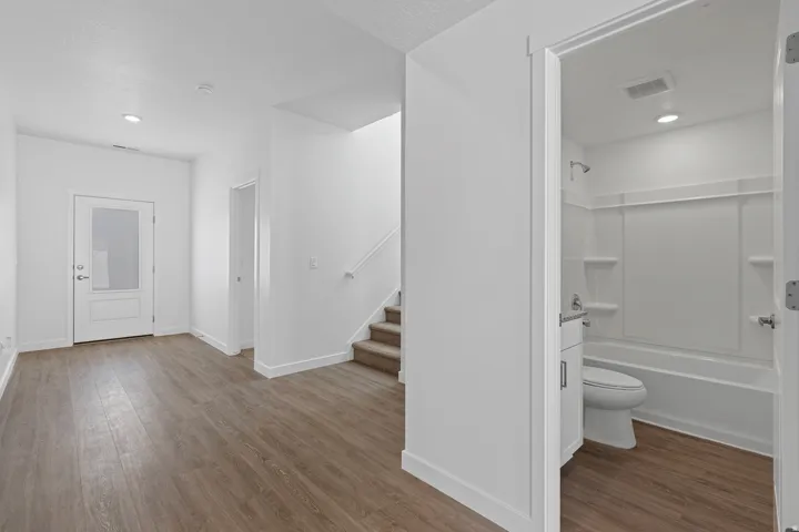 Wood-finish flooring, recessed lighting, white interior doors, staircase with carpeted treads, and a full bathroom with a tub/shower combination