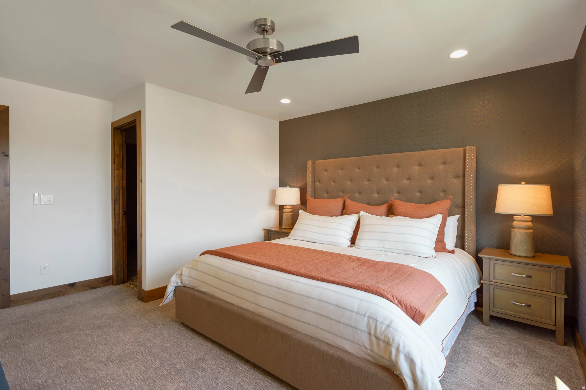 Recessed lighting, ceiling fan, brown accent wall, light wood-finish door frame, and textured carpet flooring