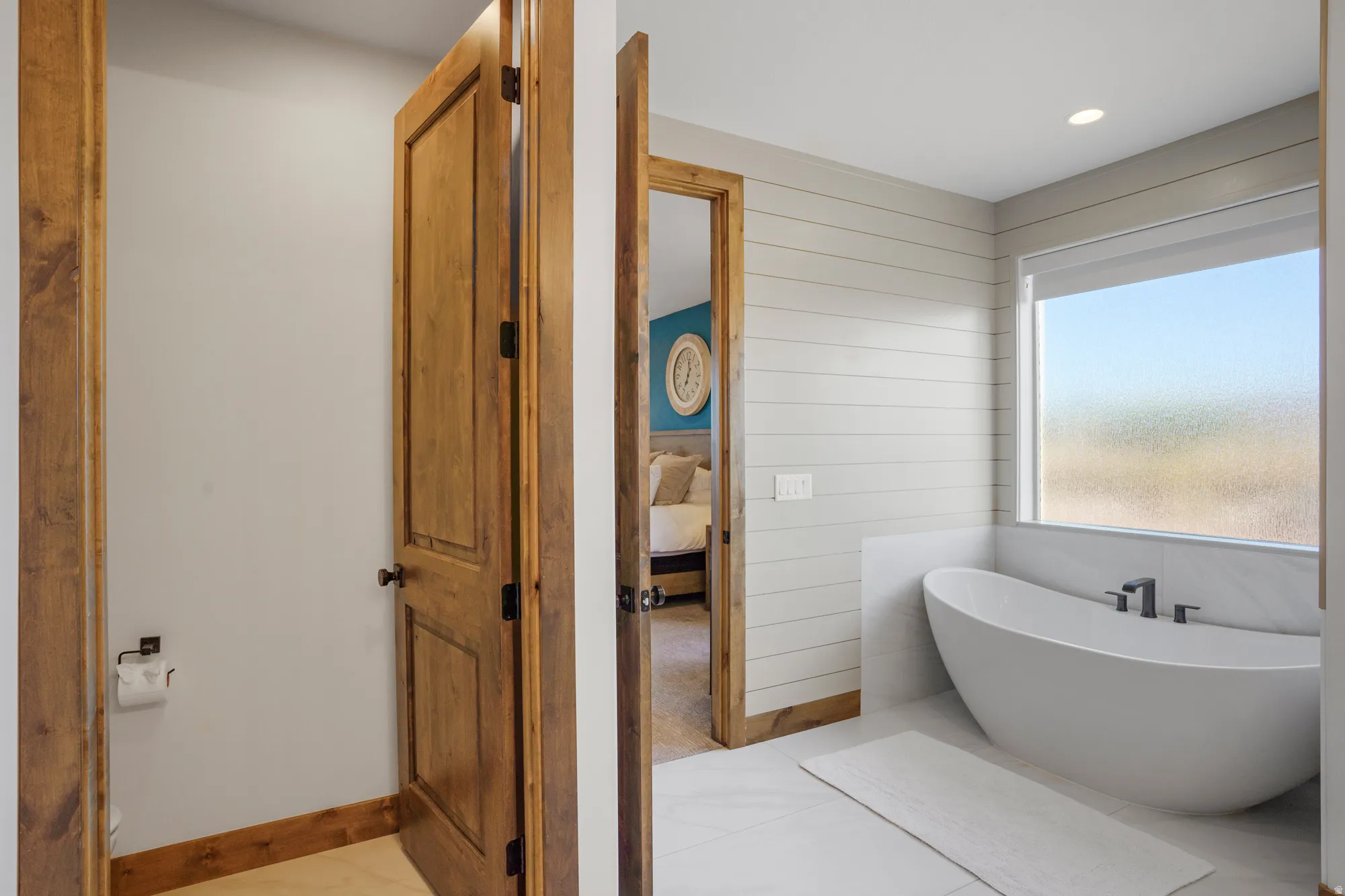 Freestanding soaking tub with dark-toned fixtures, light wood-finish door, and horizontal shiplap wall paneling