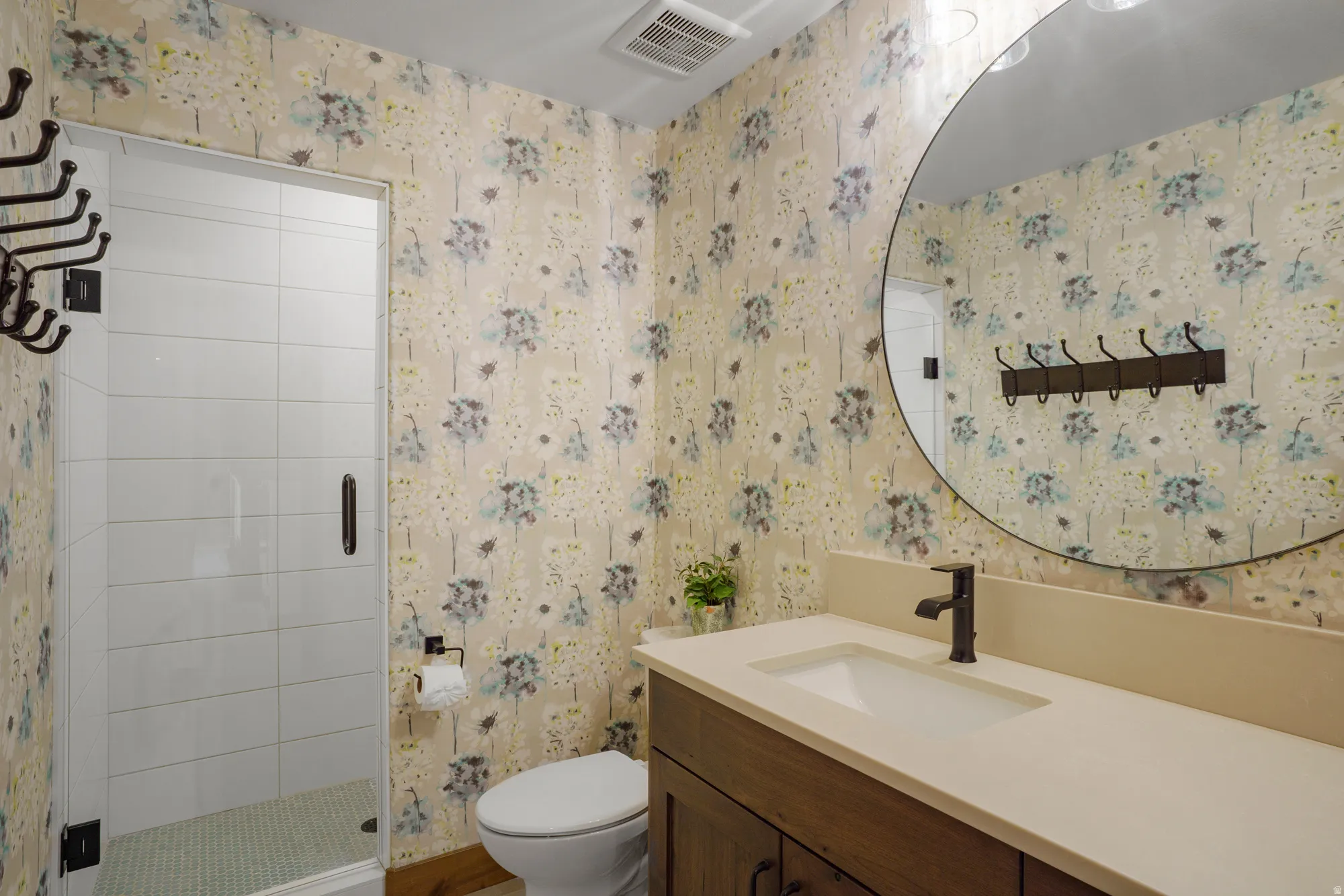 Frameless glass shower enclosure with white tiled walls, vanity with integrated sink, dark bronze-finish fixtures, and a large circular mirror