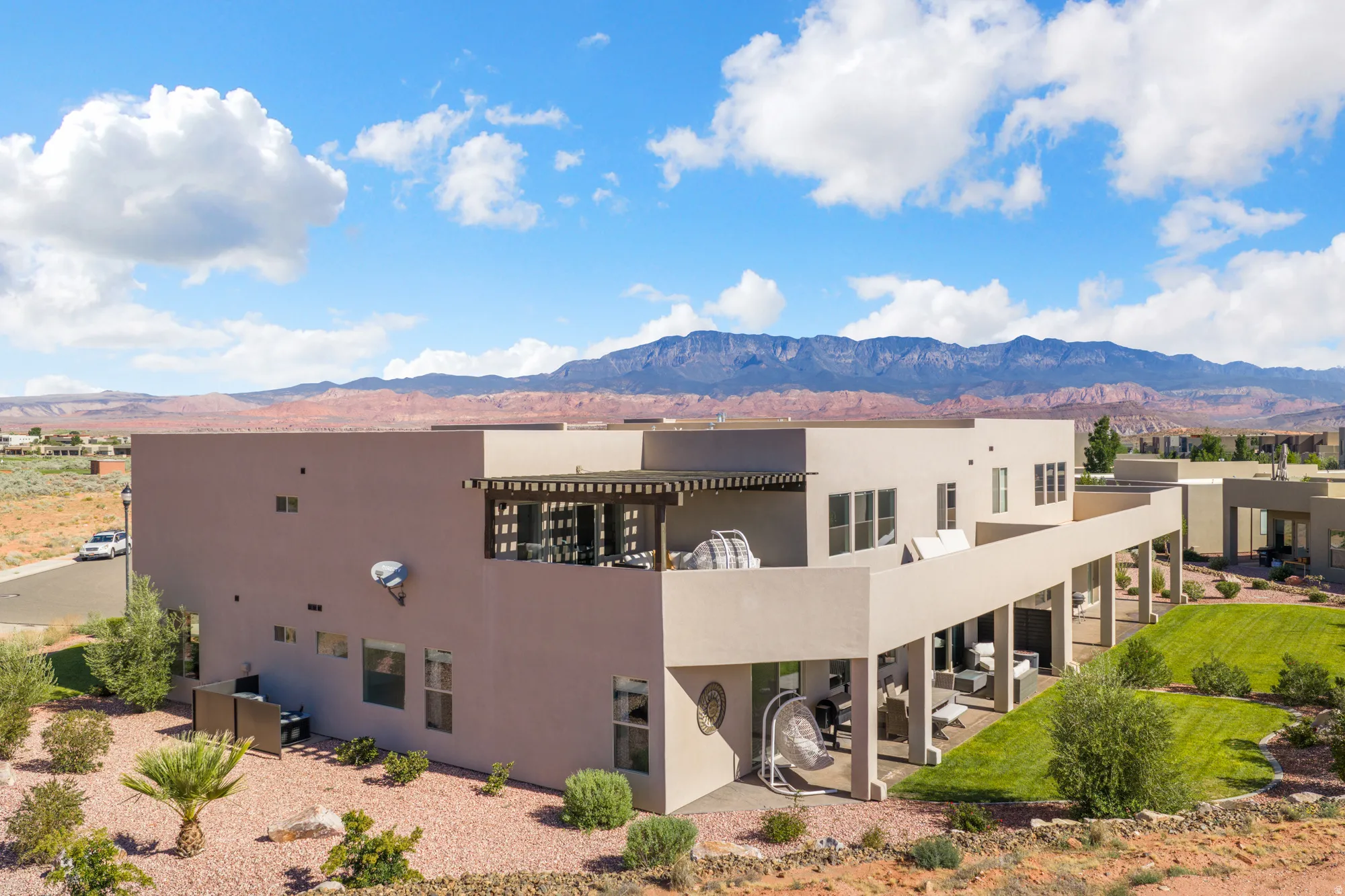 Modern stucco exterior with multiple windows, an upper-level balcony featuring a pergola, and a covered patio supported by columns