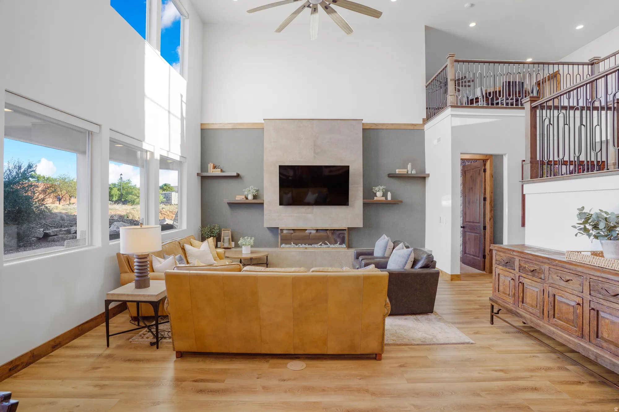 Vaulted ceilings with an exposed beam, multiple large windows, wood-finish flooring, and a contemporary fireplace with stone surround