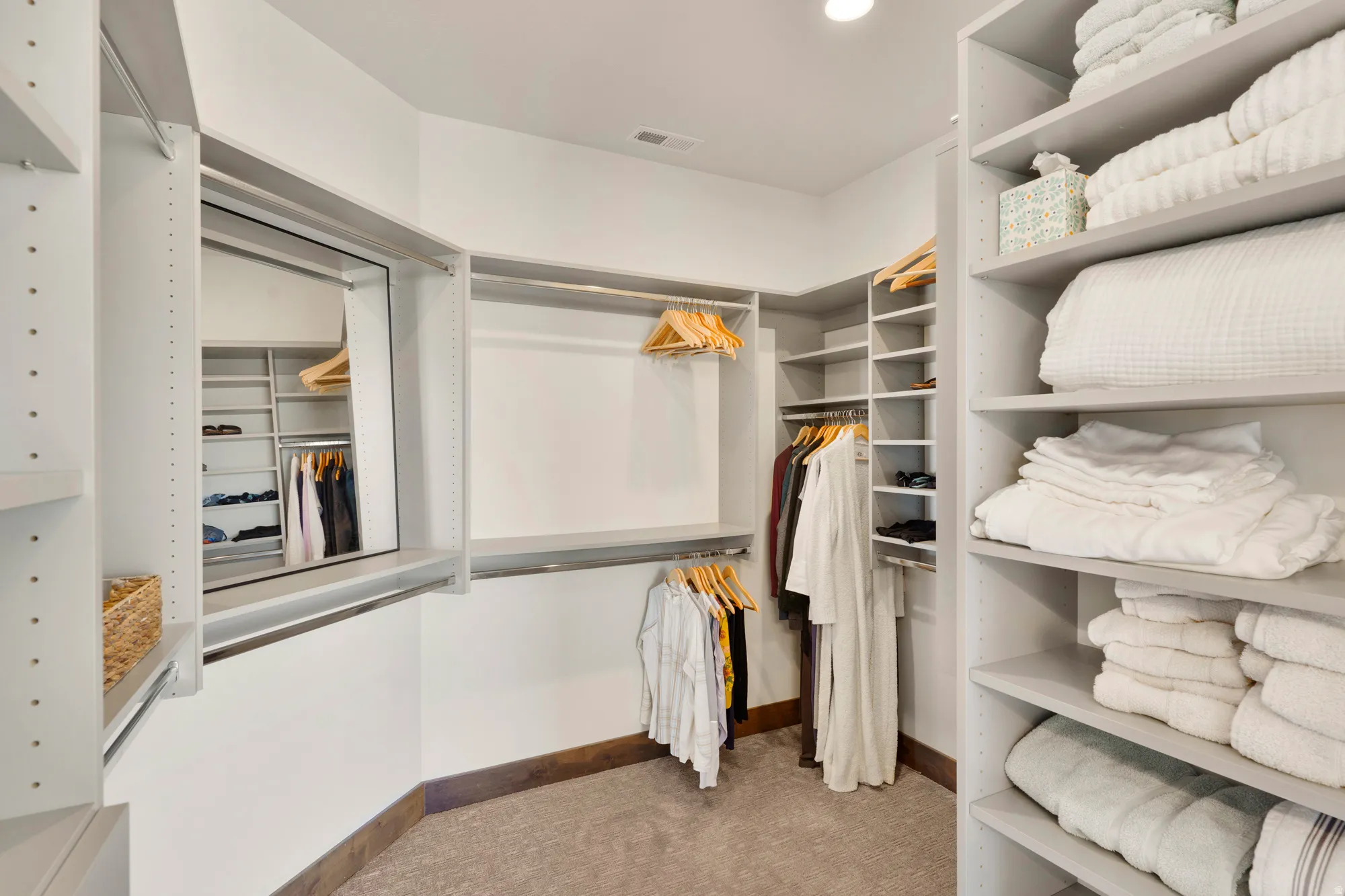 Custom closet system featuring integrated shelving, multiple hanging rods, corner shelving units, and a full-length mirror