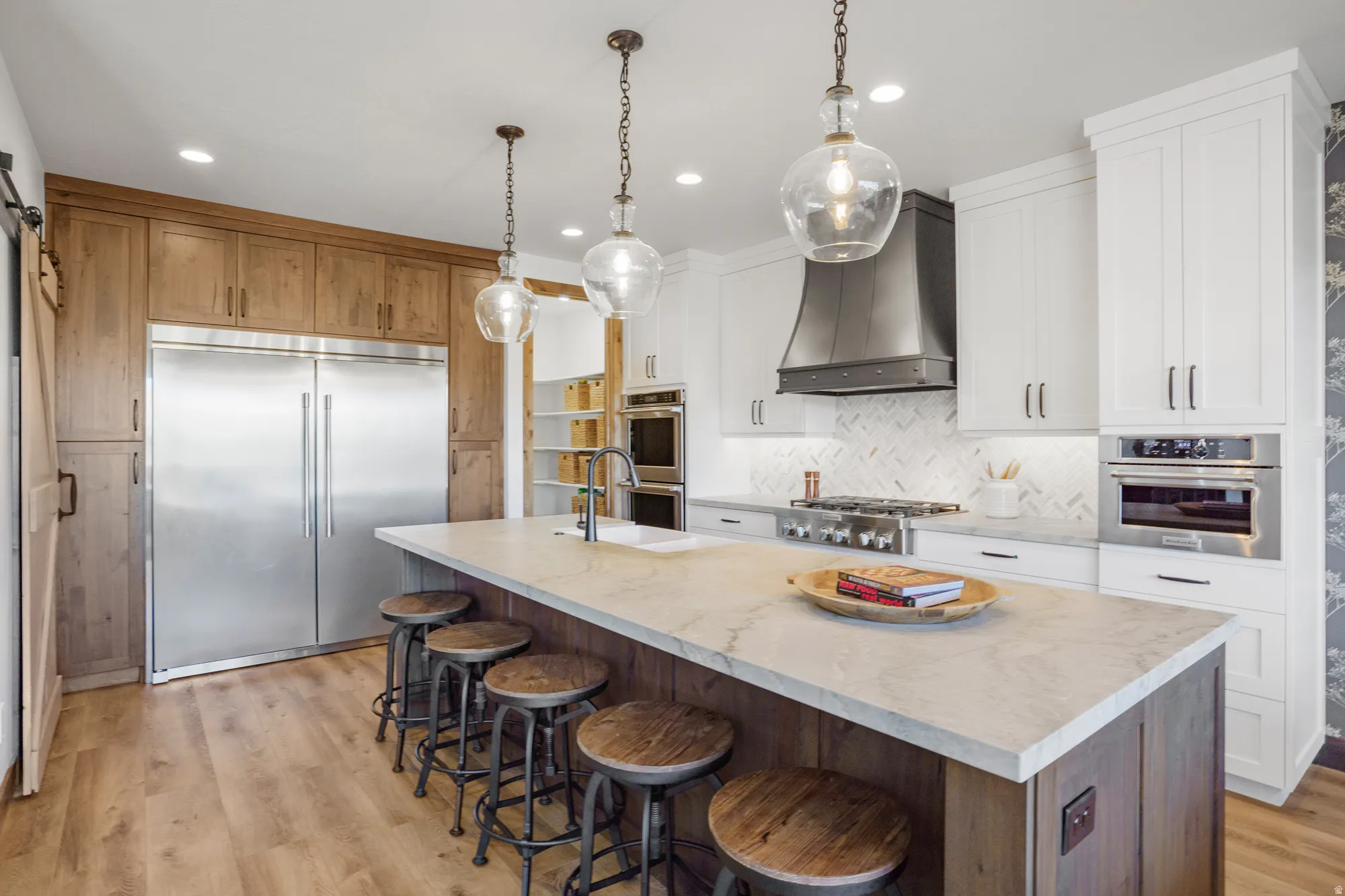 Gourmet kitchen featuring a large central island, professional-grade stainless steel appliances, custom cabinetry, herringbone tile backsplash, and wood-finish flooring