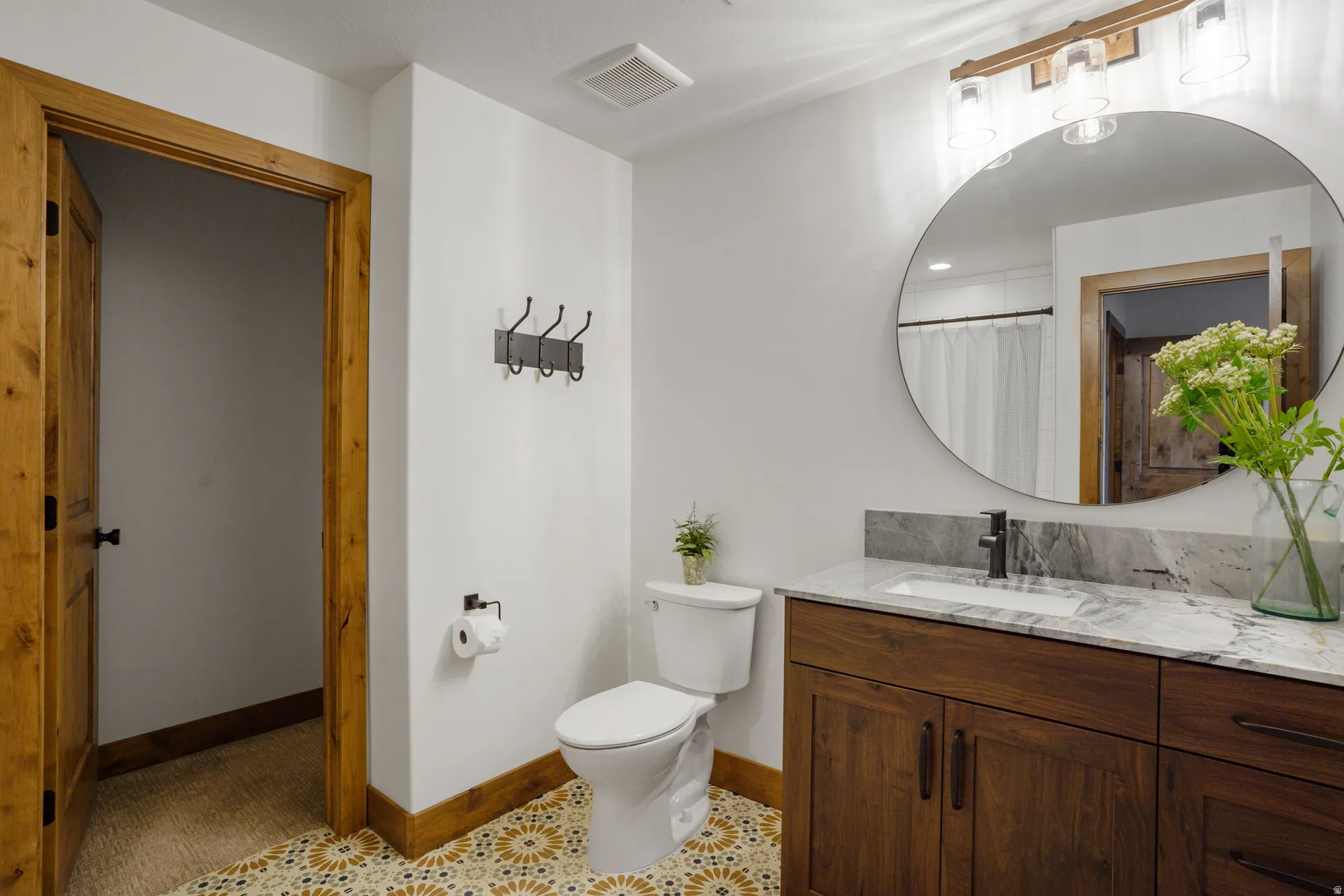 Bathroom featuring a wood-finish vanity with a light-toned countertop, a circular mirror, and patterned floor tiles