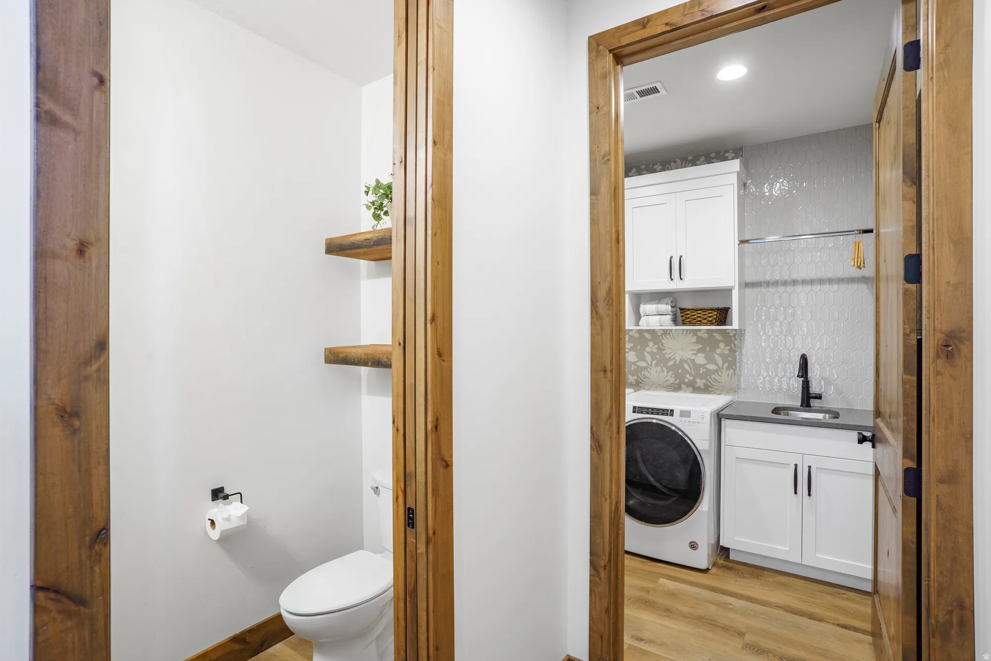 Built-in shelving, wood-finish flooring, white cabinetry, textured tile backsplash, and a utility sink with a black faucet