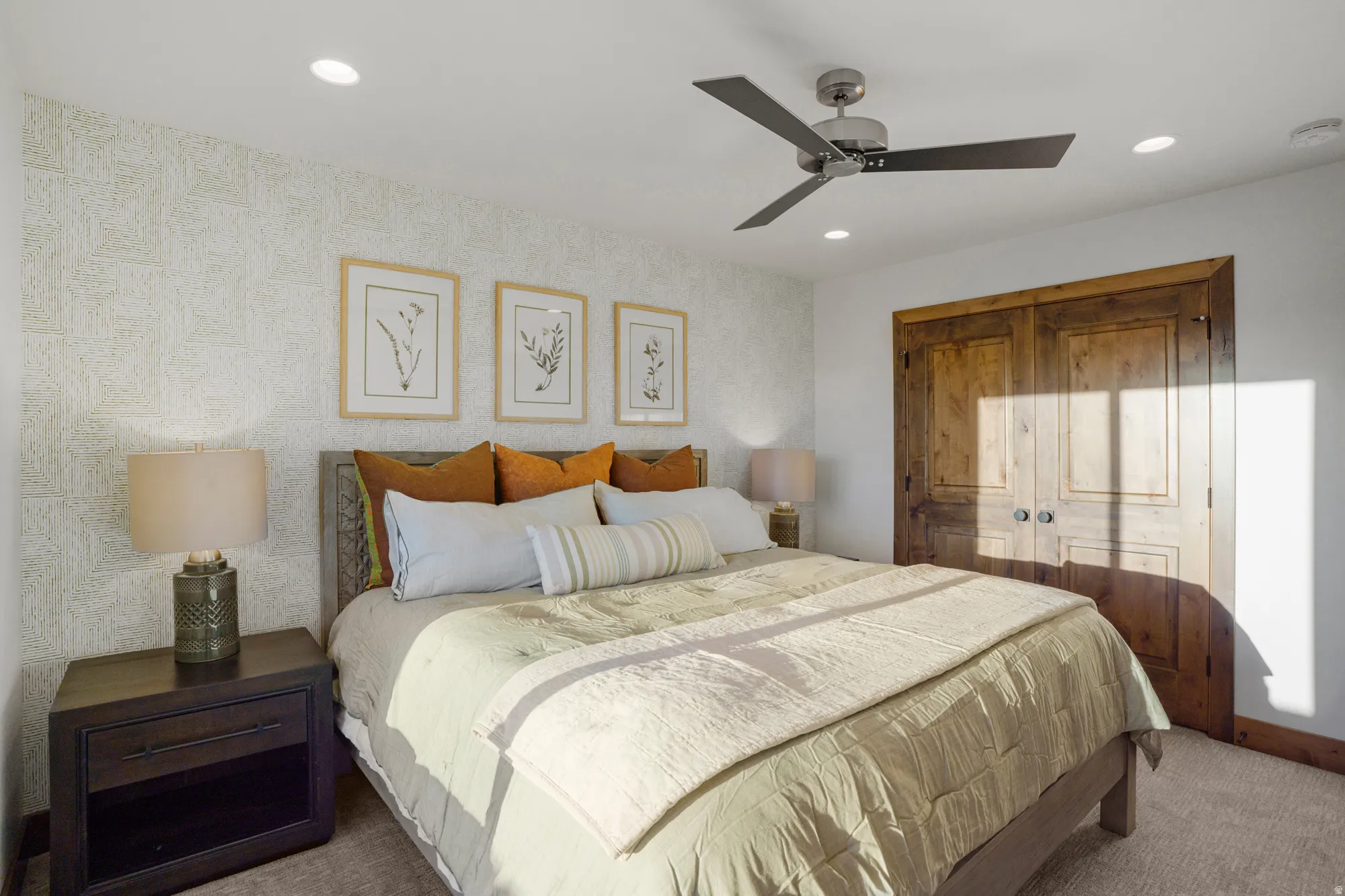 Patterned accent wall, wood panel bi-fold doors, dark wood-finish nightstand, recessed lighting, and a ceiling fan