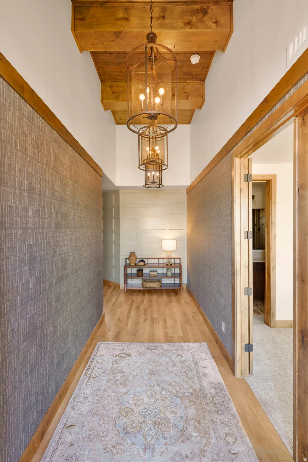 Hardwood flooring, wood-beamed ceiling, textured wall coverings, wood-frame doorway, and a tiered chandelier