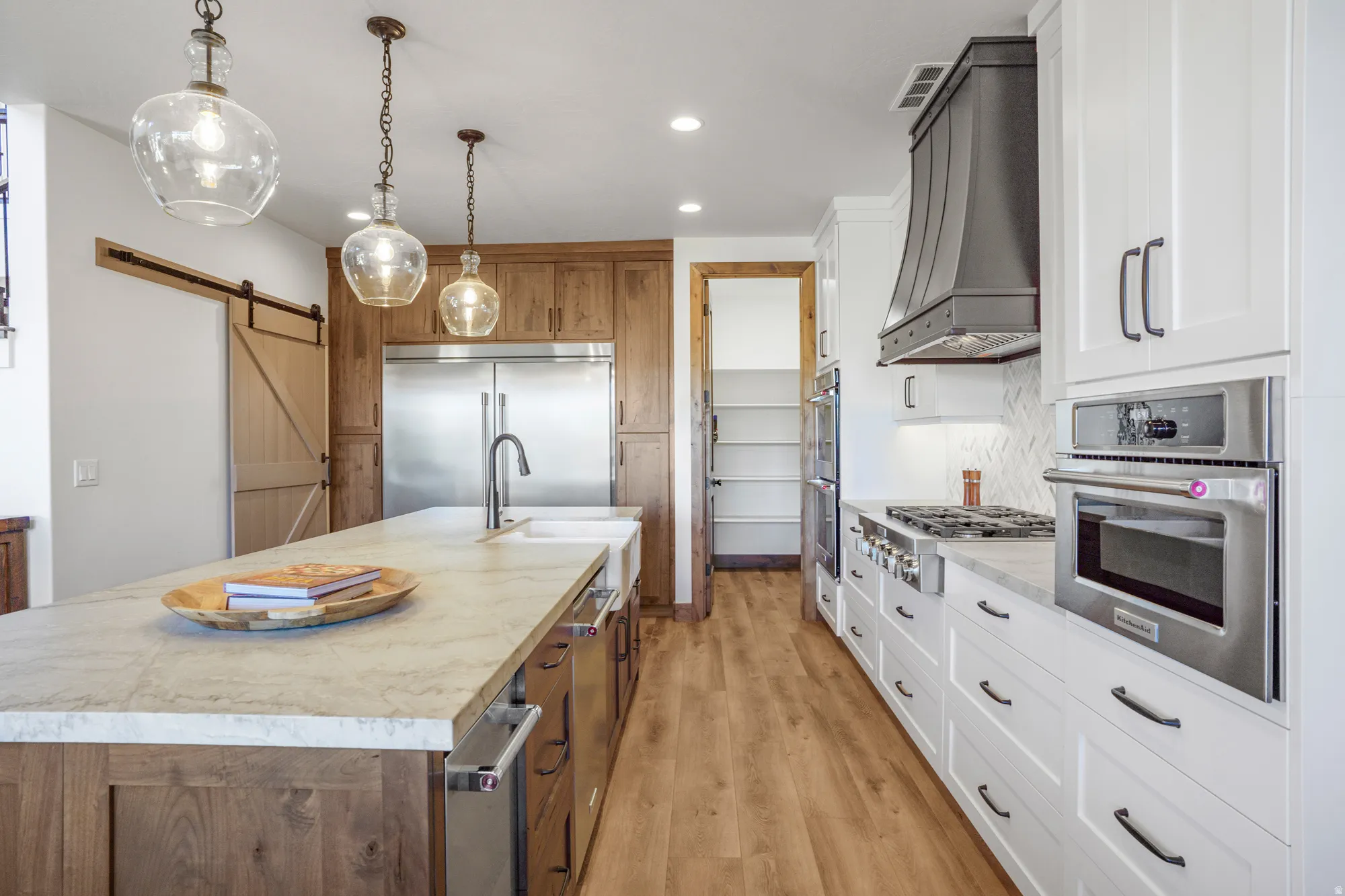 Kitchen featuring wood-finish flooring, two-tone cabinetry, stainless steel appliances, a large center island, and a barn door entry