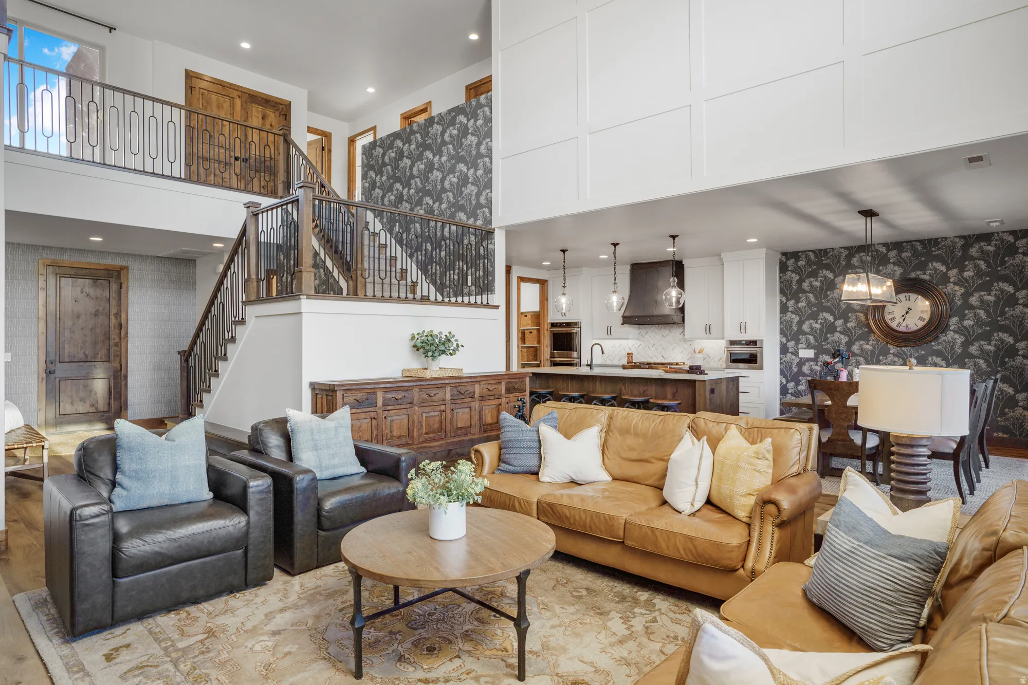 Two-story ceiling, wood-finish flooring, open-concept living area, staircase with wrought iron railing, and a kitchen with an island