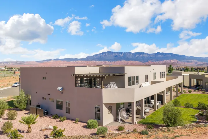 Modern stucco exterior with multiple windows, an upper-level balcony featuring a pergola, and a covered patio supported by columns