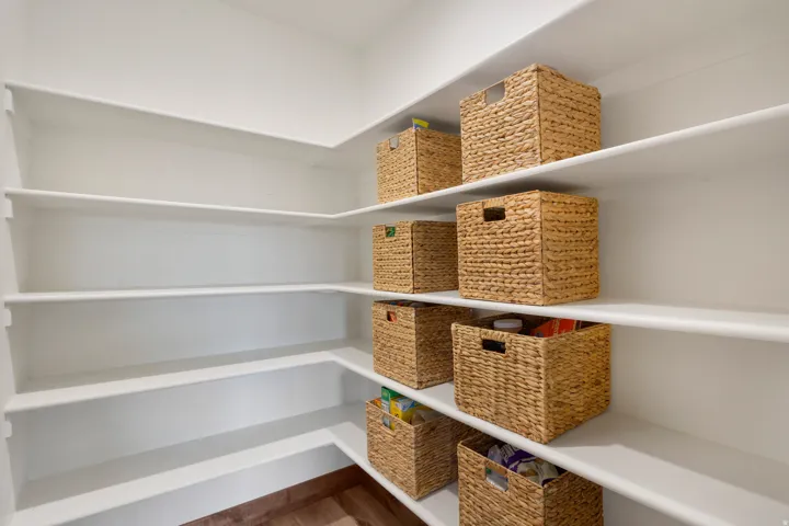 L-shaped pantry with white shelving and wood-finish flooring