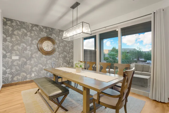 Hardwood-finish flooring, accent wall with botanical pattern, contemporary rectangular chandelier, and expansive sliding glass doors