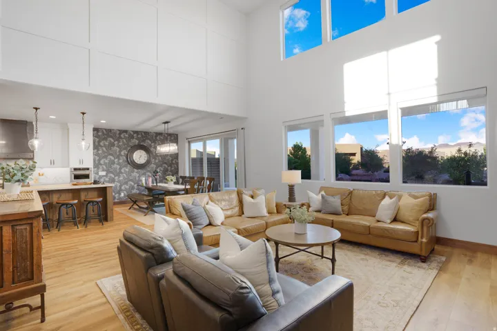 Two-story living area with high ceilings, large windows, wood-finish flooring, and an open-concept kitchen with a breakfast bar