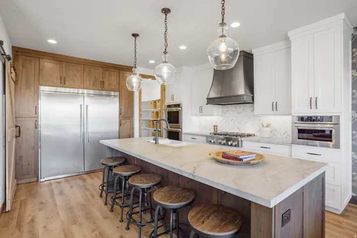 Gourmet kitchen featuring a large central island, professional-grade stainless steel appliances, custom cabinetry, herringbone tile backsplash, and wood-finish flooring