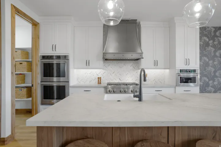 White shaker cabinetry, stainless steel double ovens, a herringbone tile backsplash, a gas range, and a large island with a surface-mounted sink