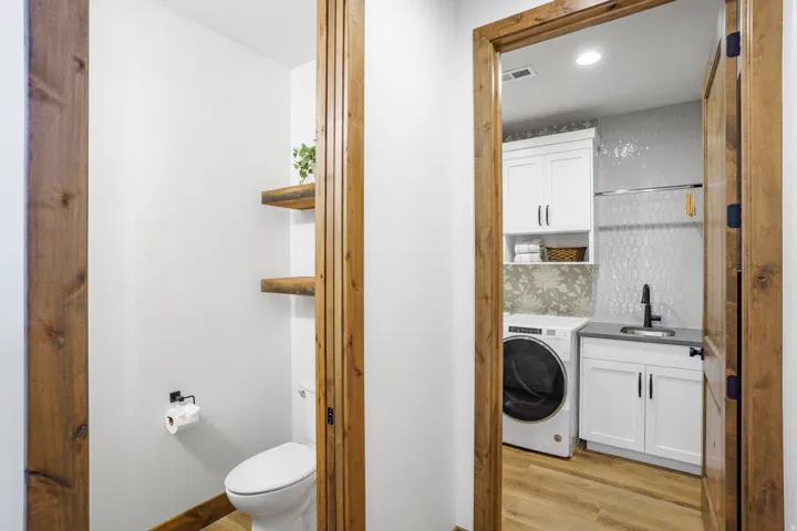 Built-in shelving, wood-finish flooring, white cabinetry, textured tile backsplash, and a utility sink with a black faucet