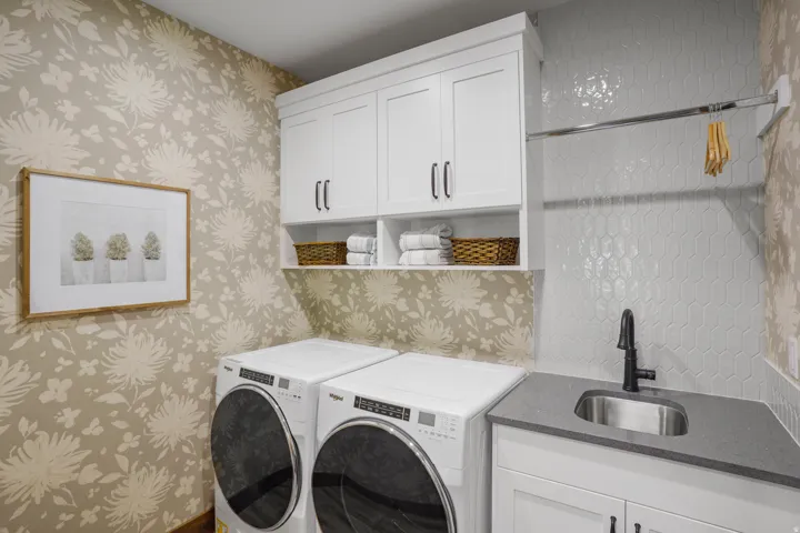 White shaker cabinetry with black hardware, hexagon tile backsplash, stainless steel sink with matte black faucet, and patterned wall covering