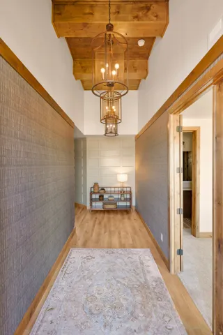 Hardwood flooring, wood-beamed ceiling, textured wall coverings, wood-frame doorway, and a tiered chandelier