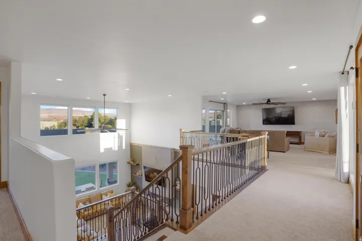 Expansive open-concept upper level with recessed lighting, carpeted flooring, and a decorative wrought iron and wood railing