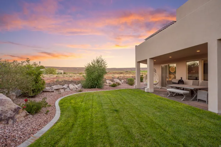 Expansive lawn bordered by a rock-lined garden bed, covered patio with recessed lighting, and sliding glass door access