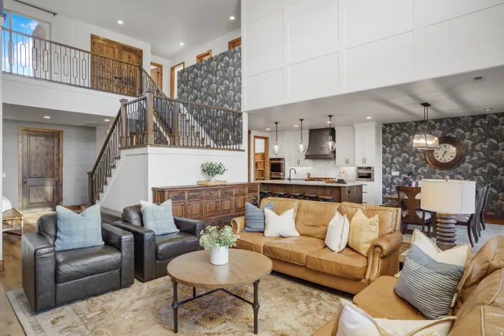 Two-story ceiling, wood-finish flooring, open-concept living area, staircase with wrought iron railing, and a kitchen with an island