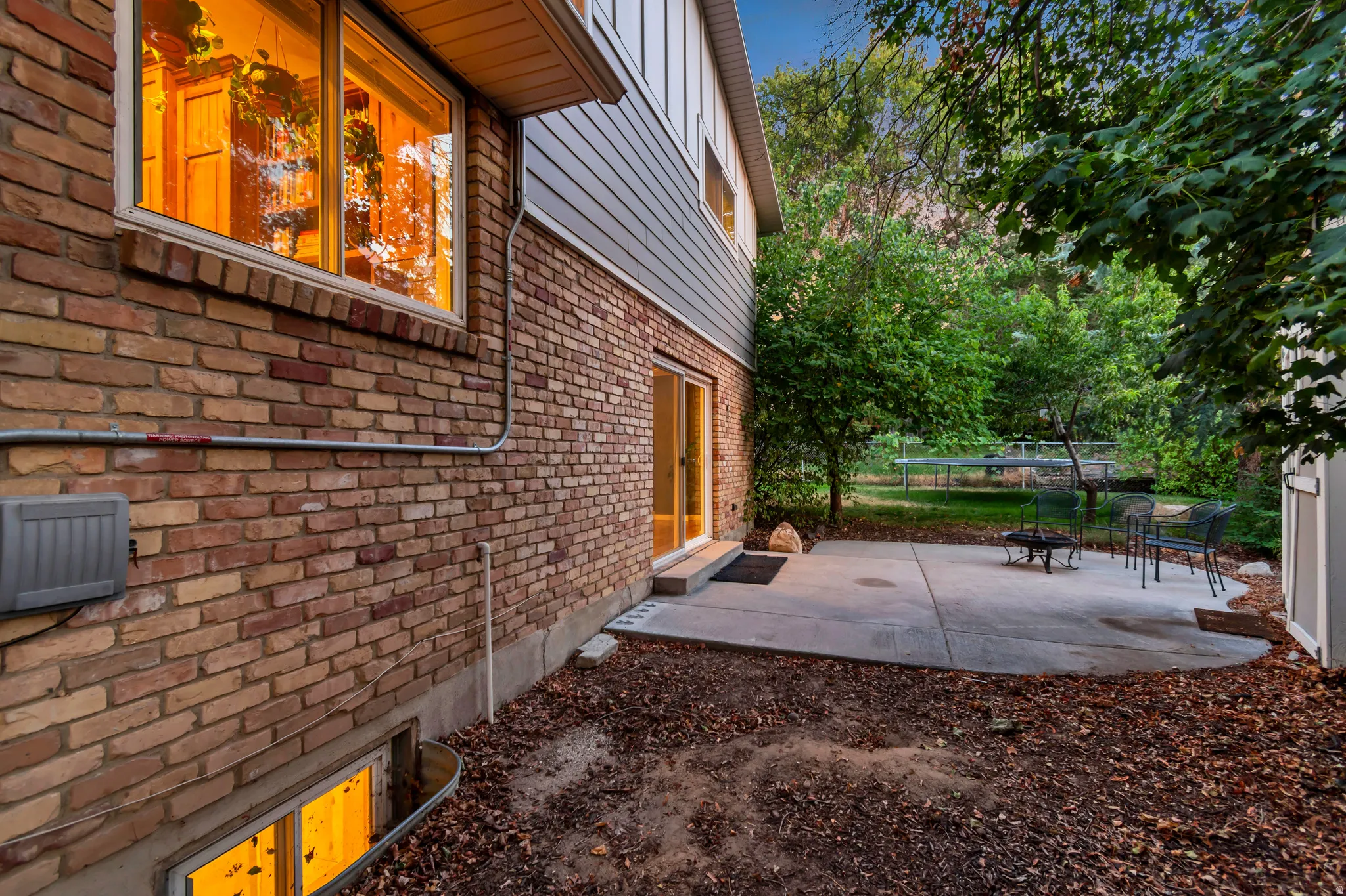 Exterior brick and siding facade with a ground-level patio and mature trees