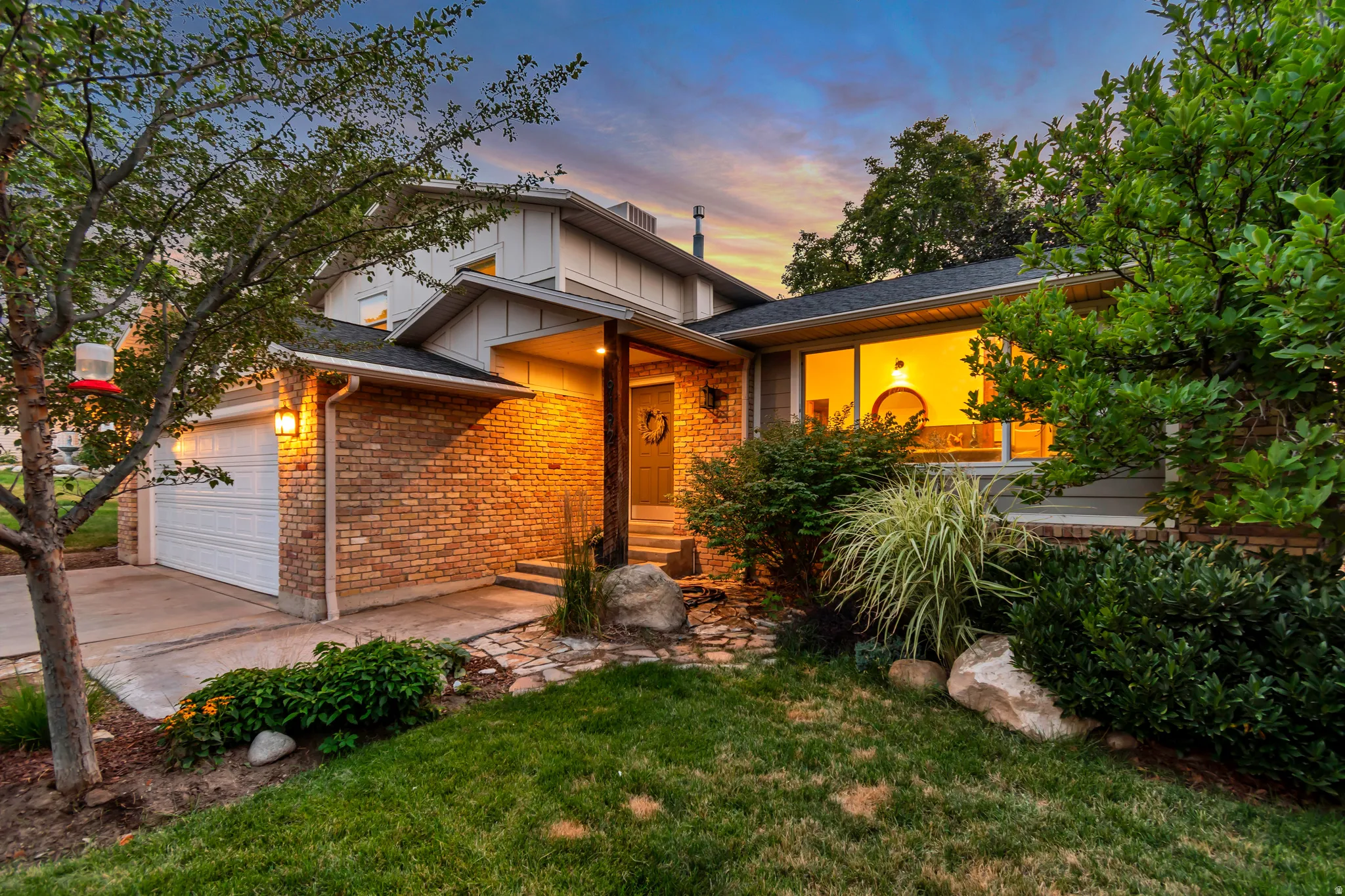 Brick and siding exterior featuring a covered entry, attached garage, and established landscaping
