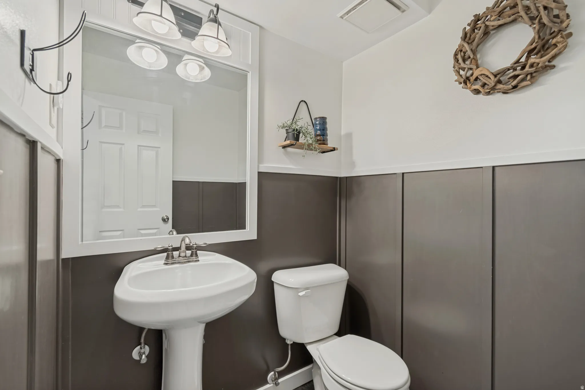 Pedestal sink with chrome faucet, framed mirror, and wall-mounted vanity lighting