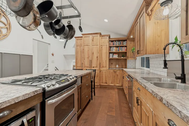 Wood-finish flooring, light wood cabinetry, stainless steel appliances, white subway tile backsplash, and a black gooseneck faucet