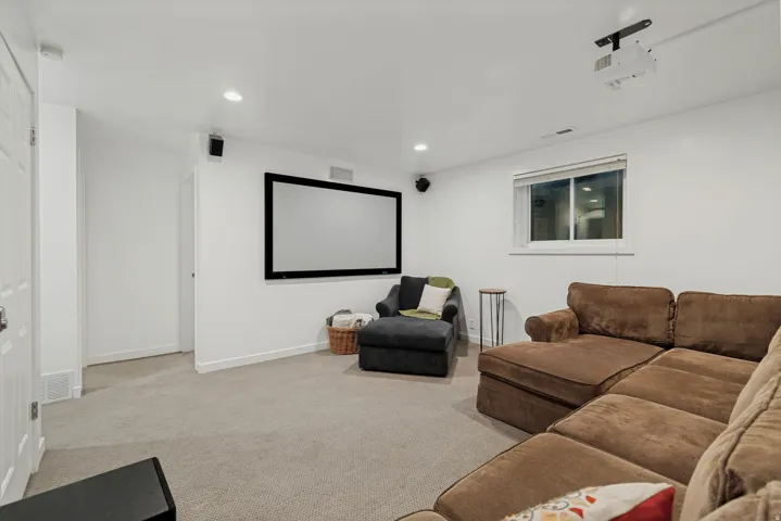 Integrated projection screen, ceiling-mounted projector, recessed lighting, wall-mounted speakers, and a window for natural light