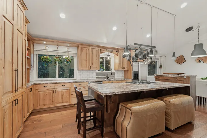 Custom wood cabinetry, granite countertops, white subway tile backsplash, wood-finish flooring, and recessed lighting