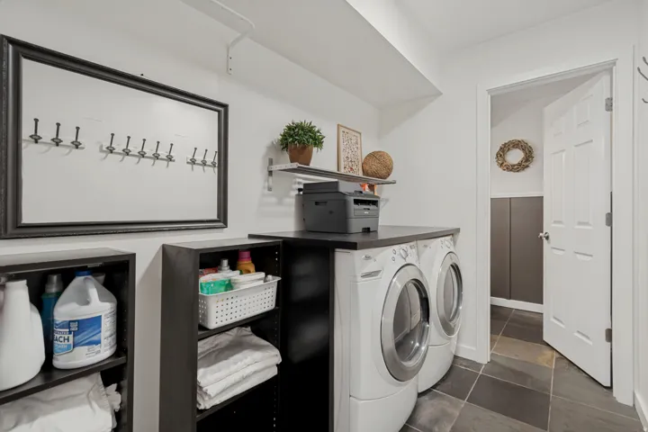 Front-loading washer and dryer, dark countertop, built-in shelving, dark tile flooring, and a paneled door
