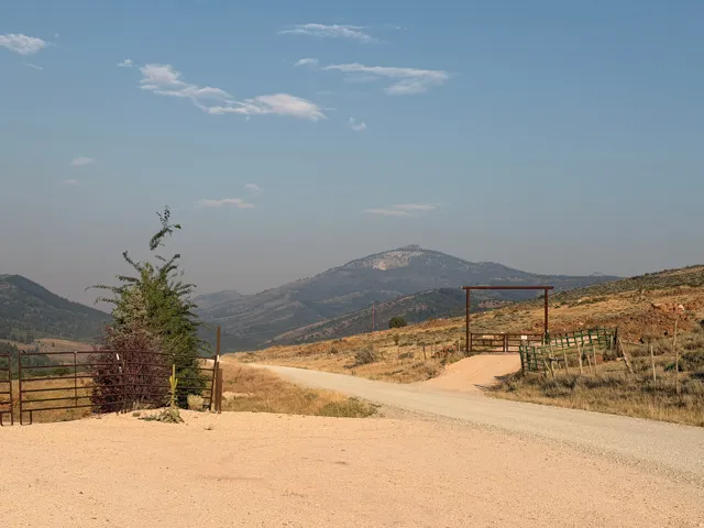 Gravel driveway approaching a metal gate entry, with distant mountain scenery