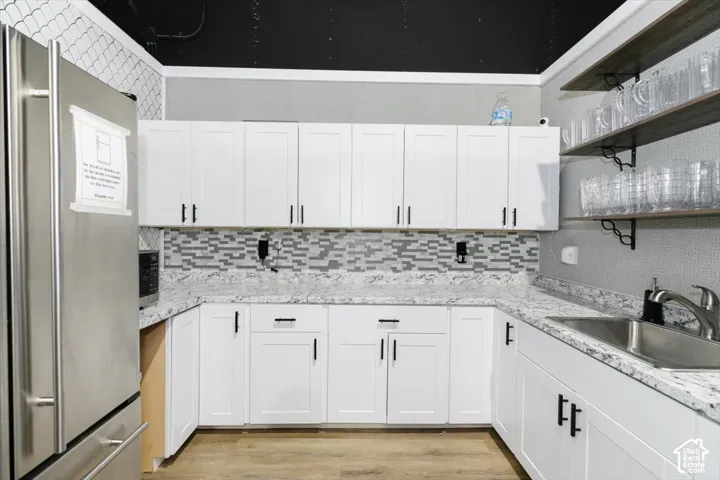 White shaker-style cabinetry with matte black hardware, mosaic tile backsplash, light-toned countertops, and wood-finish flooring